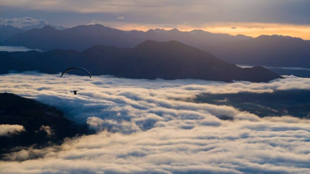 A skydiver flying over clouds and mountains in the sunset