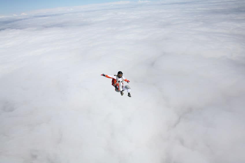 A skydiver in white and orange professional gear, falling out of control in the air.