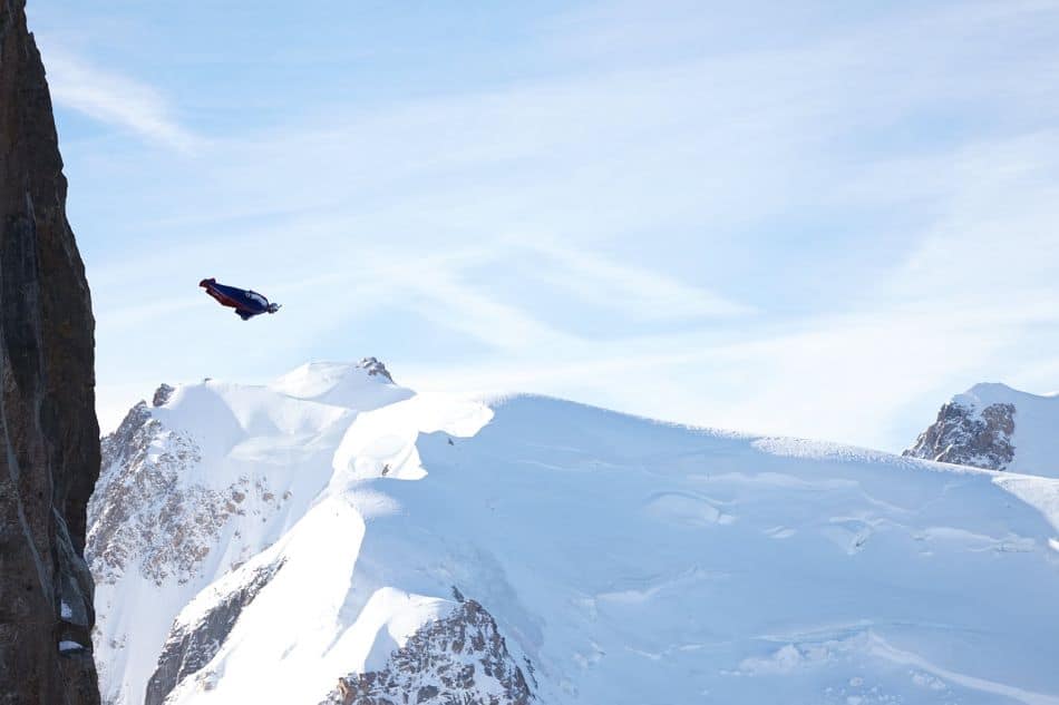 A wingsuit pilot in a blue wingsuit flying over a snowy mountain landscape.