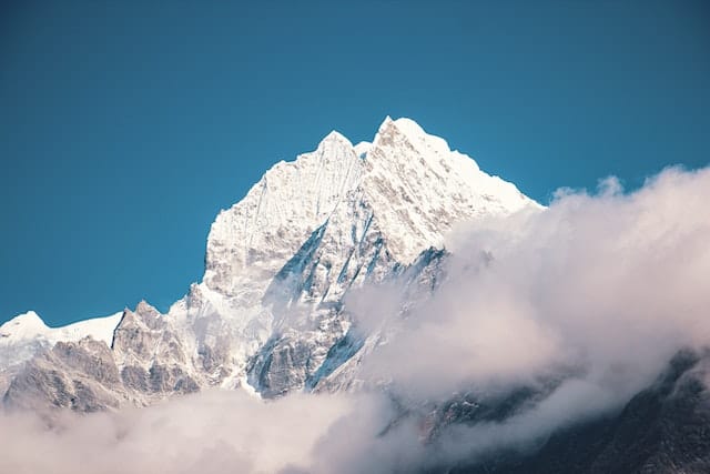A majestic snow-capped mountain peak piercing through a blanket of fluffy white clouds against a serene blue sky.