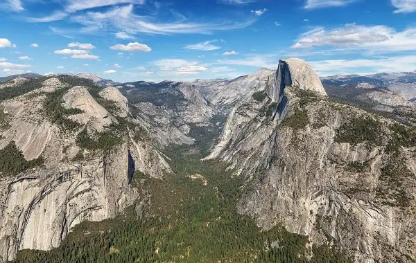 A breathtaking view of Yosemite Valley, showcasing the iconic Half Dome, vast forests, and rugged mountain terrain under a clear blue sky.